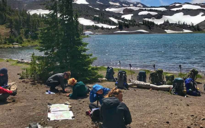 a group of students rest best an alpine lake on an outward bound course